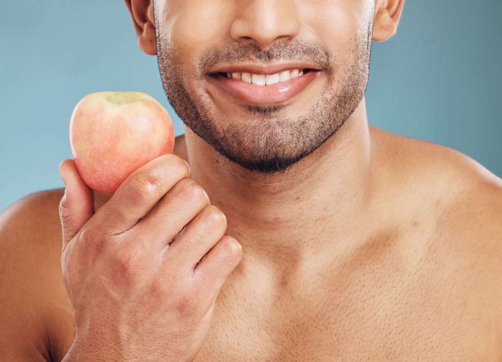 Visage, soins de la peau et homme avec une pomme pour la santé, la vitamine c et la nutrition sur fond bleu de studio